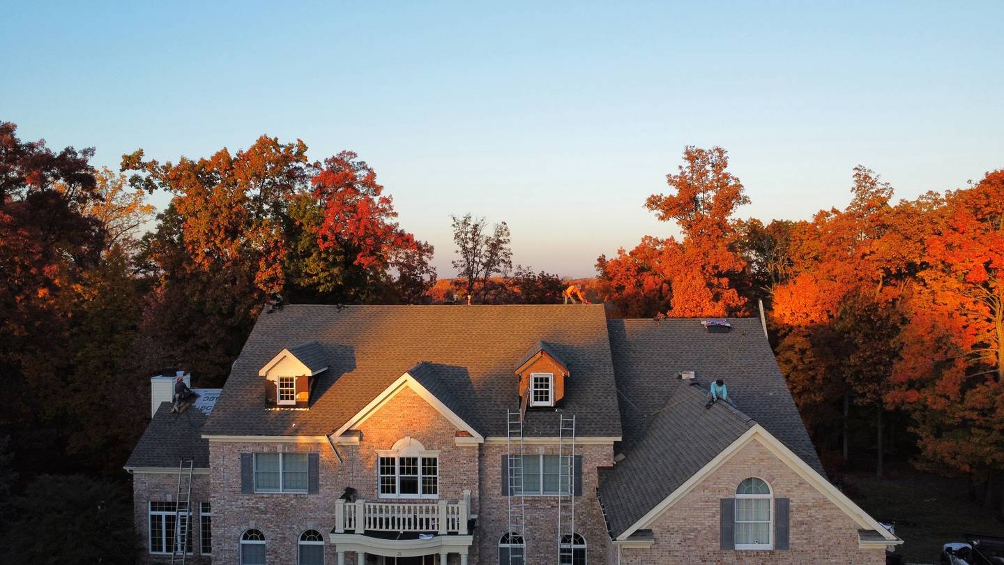 Brick colonial with new shingles on the roof at sunset, two crew members still working up top