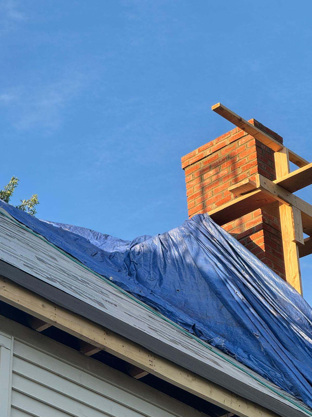 Brick chimney with wood bracing and a blue tarp covering the roof beside it