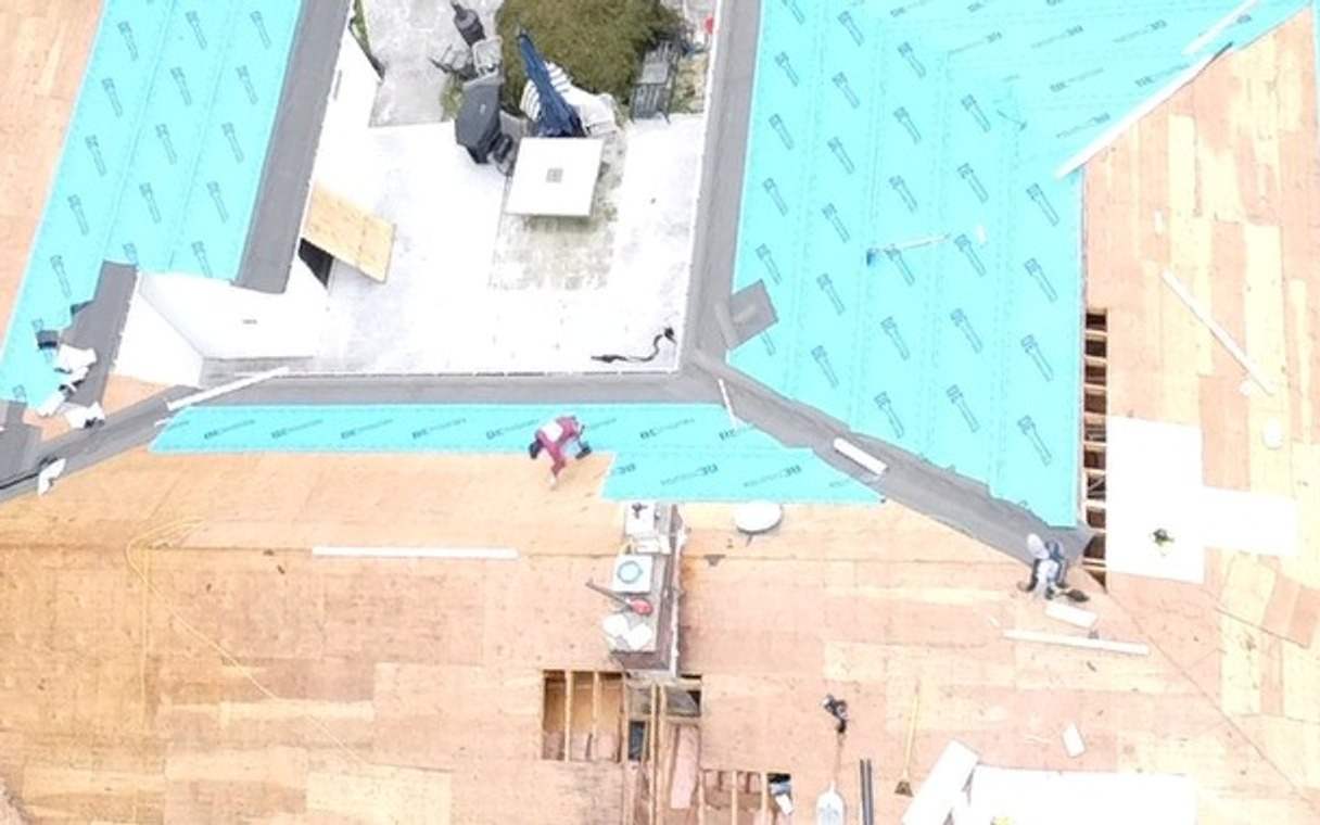 The same house from the pool side: old shingles removed, new plywood decking and the first rows of blue underlayment
