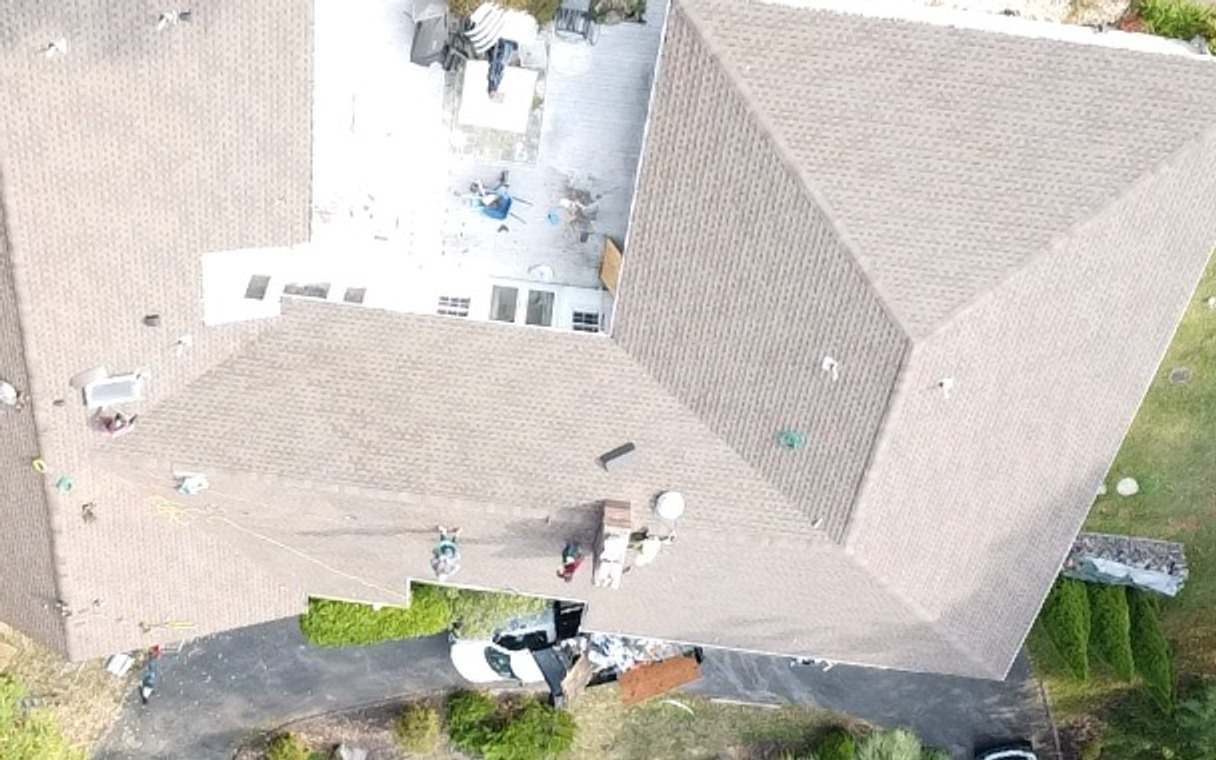 Drone view of an L-shaped house with its old tan shingle roof and a covered pool, rotated to line up with the next two shots