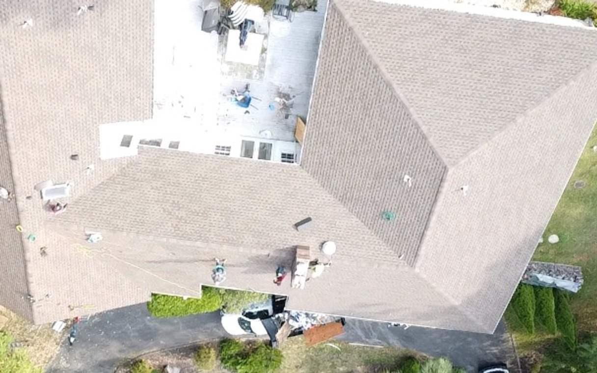 Drone view of an L-shaped house with its old tan shingle roof and a covered pool, rotated to line up with the next two shots